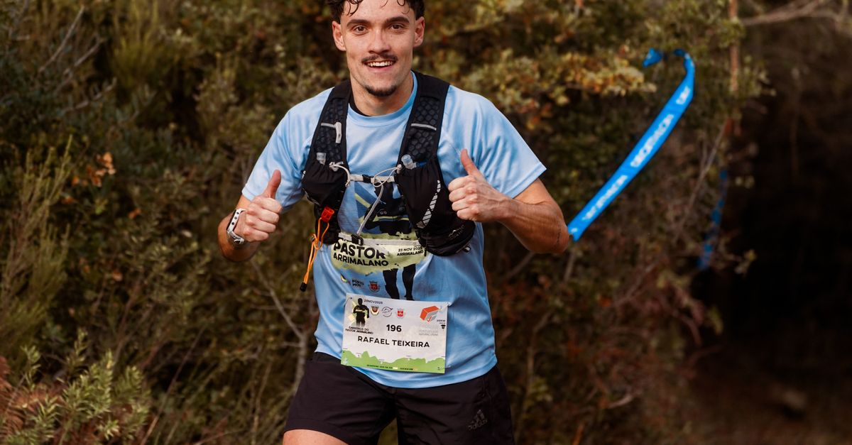 Young male trail runner enthusiastically giving a thumbs up during an outdoor race through forest.